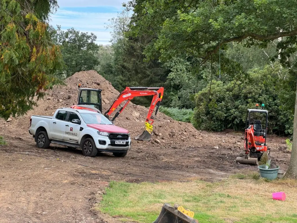 Swiss Build excavators and a branded pickup beside excavated soil on site.