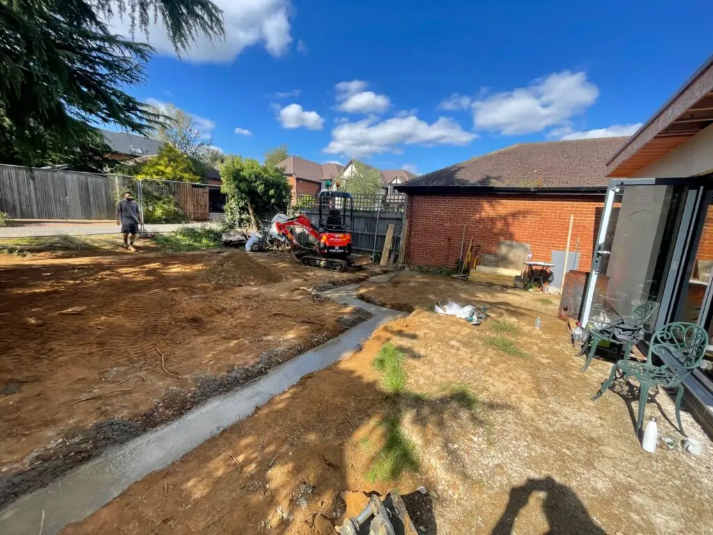A Swiss Build mini digger beside prepared ground and concrete foundation trenches.