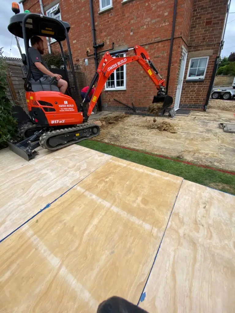 Swiss Build’s mini digger excavating beside a house with boards protecting the garden access.