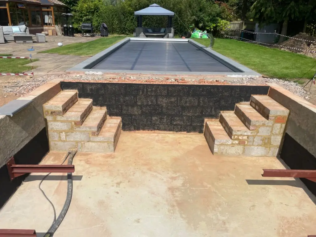 Prepared outdoor ground with blockwork steps and an existing covered pool beyond.
